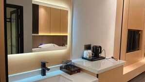 A modern bathroom with a large mirror, a sink, a coffee maker, and a towel rack. - Dongfang Guanda Business Hotel (Dongfang)
