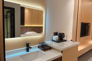 A modern bathroom with a large mirror, a sink, a coffee maker, and a towel rack.