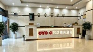 A hotel reception area with a reception desk, potted plants, and a digital display above the desk. - Dongfang Guanda Business Hotel (Dongfang)