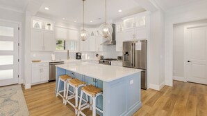 A spacious kitchen with a large island, white cabinetry, stainless steel appliances, and hanging pendant lights. - Brand New 6BR/6BA Luxury, 20min to Clemson. Wooded flat lot/firepit/pool table! (West Union)