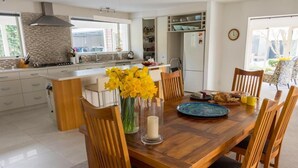 Una cocina moderna con armarios blancos, una isla central y un comedor con sillas de madera y una mesa lista para el desayuno.