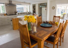 Una cocina moderna con armarios blancos, una isla central y un comedor con sillas de madera y una mesa lista para el desayuno.