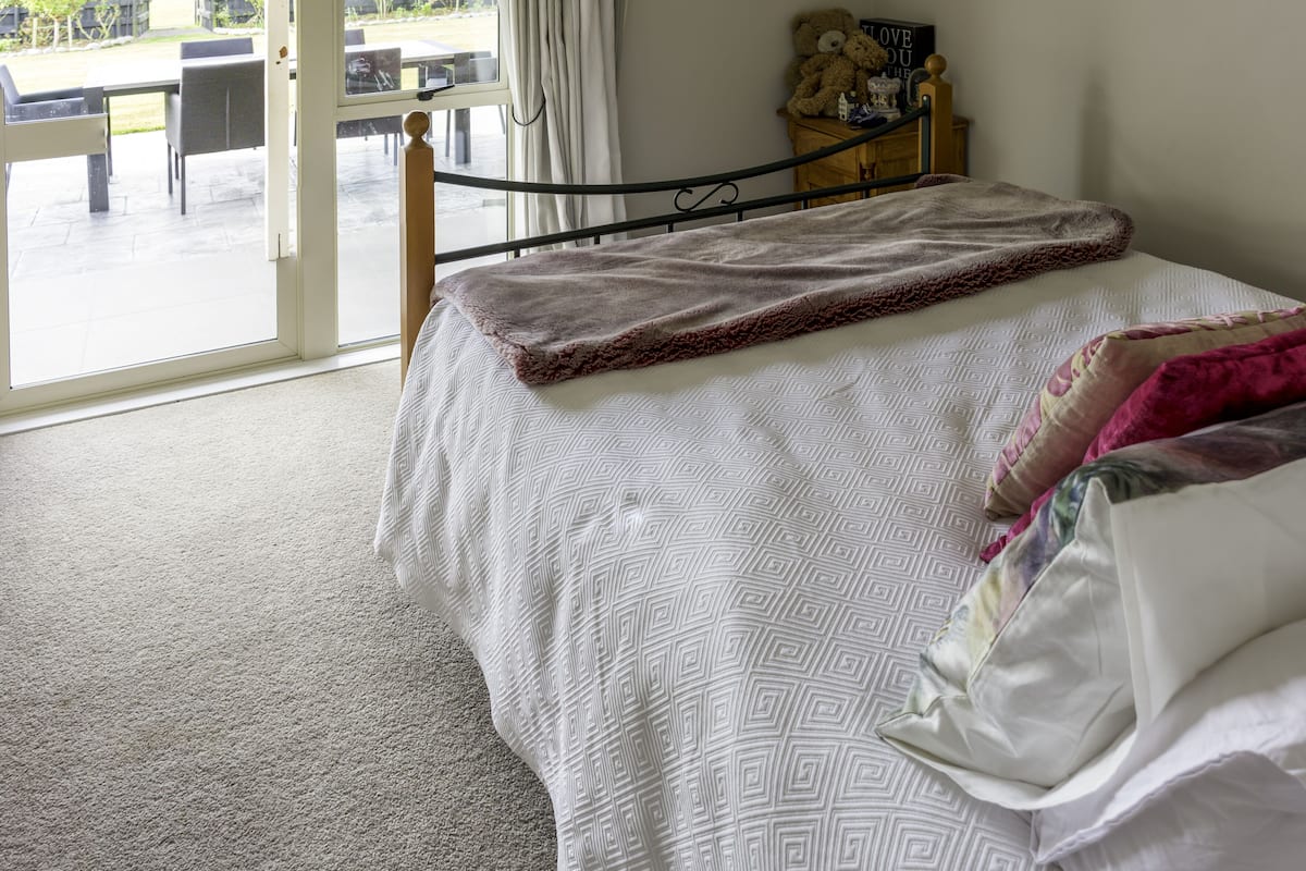 A bedroom with a bed, a view of the outdoors, and a small table with a teddy bear.