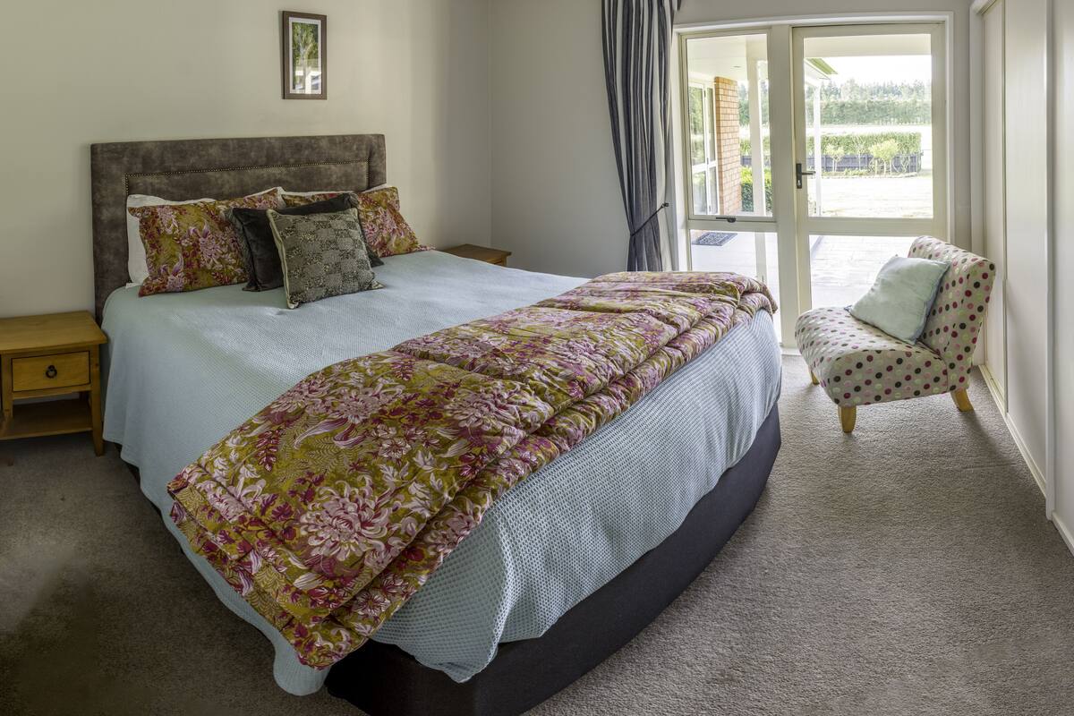 A bedroom with a large bed, a nightstand, a chair, and a view through a glass door.