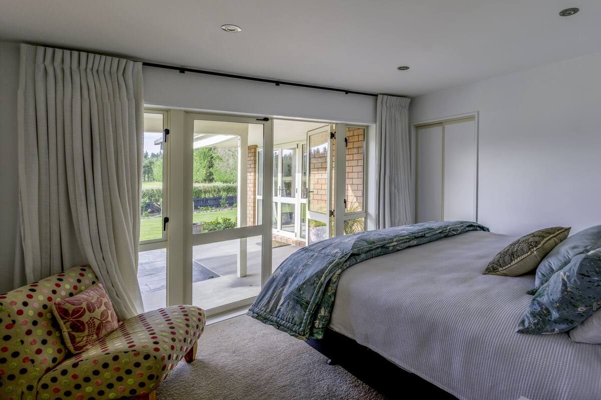 A bedroom with a large bed, a chair, and a sliding glass door leading to a patio.