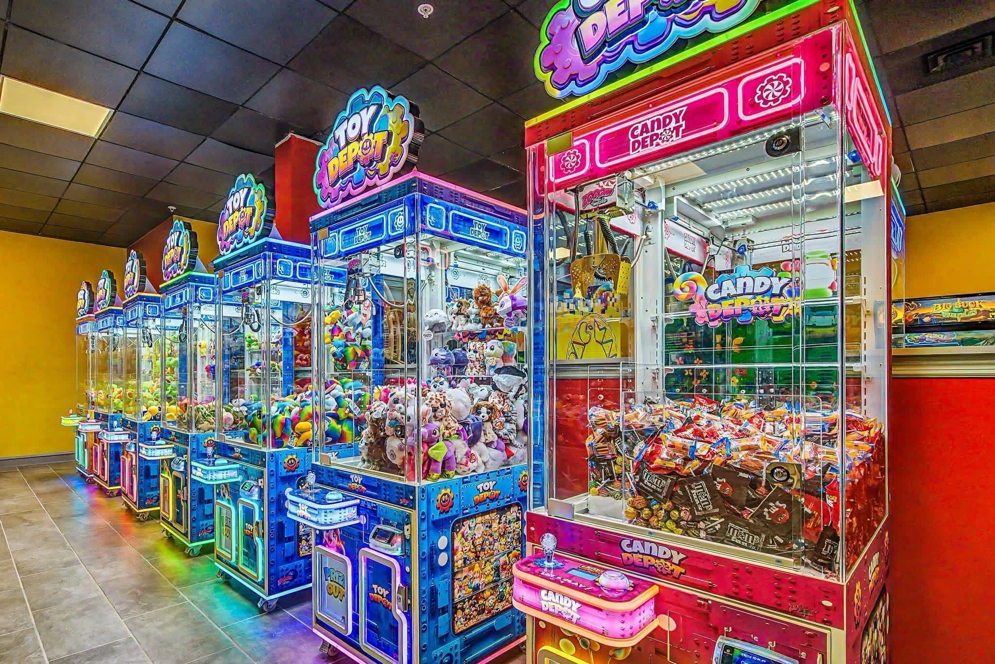 Uma fileira de máquinas de jogos eletrônicos brilhantes, incluindo jogos de garra, com um Candy Depot.