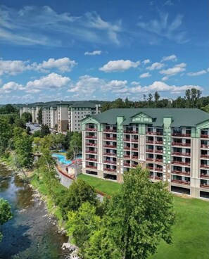 Un hôtel à plusieurs étages doté de balcons, d’une piscine et d’une rivière en premier plan.