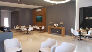 A modern reception area with a wooden reception desk, white chairs, and a large screen on the wall. - Urquiza Suites Salta (Salta)