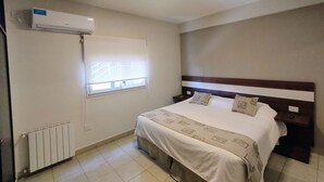 A bedroom with a bed, a window with blinds, a radiator, and an air conditioning unit. - Urquiza Suites Salta (Salta)