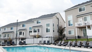 A residential building with a swimming pool, lounge chairs, and a fenced area.