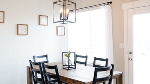 A dining area with a wooden table and black chairs, a hanging light fixture, and framed pictures on the wall.