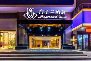 The exterior of a hotel with a prominent sign, a covered entrance, and a well-lit facade. - Magnotel Classic Xining high-speed railway station Dashizi Mojia street Hotel (Xining)