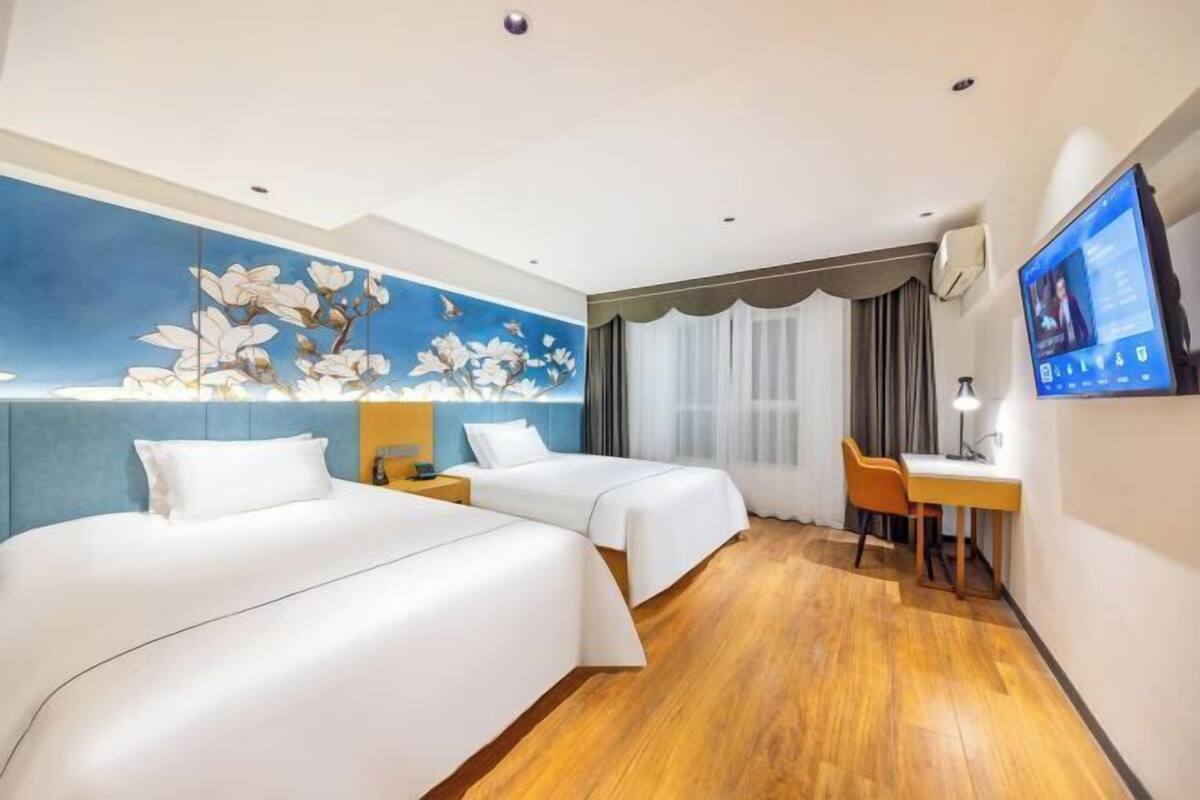 A hotel room with two beds, a desk, a TV, and a mural on the wall.