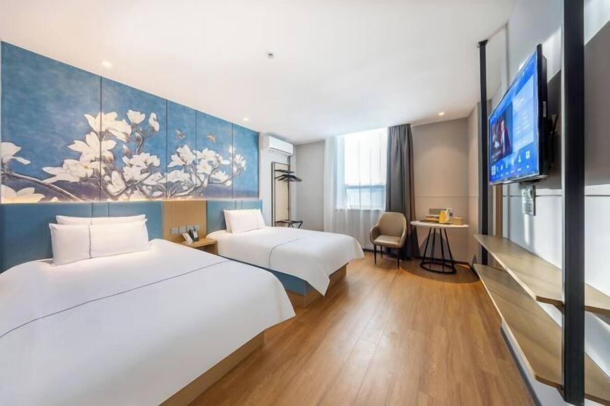 A hotel room with two beds, a TV, a desk, and a large floral artwork on the wall.