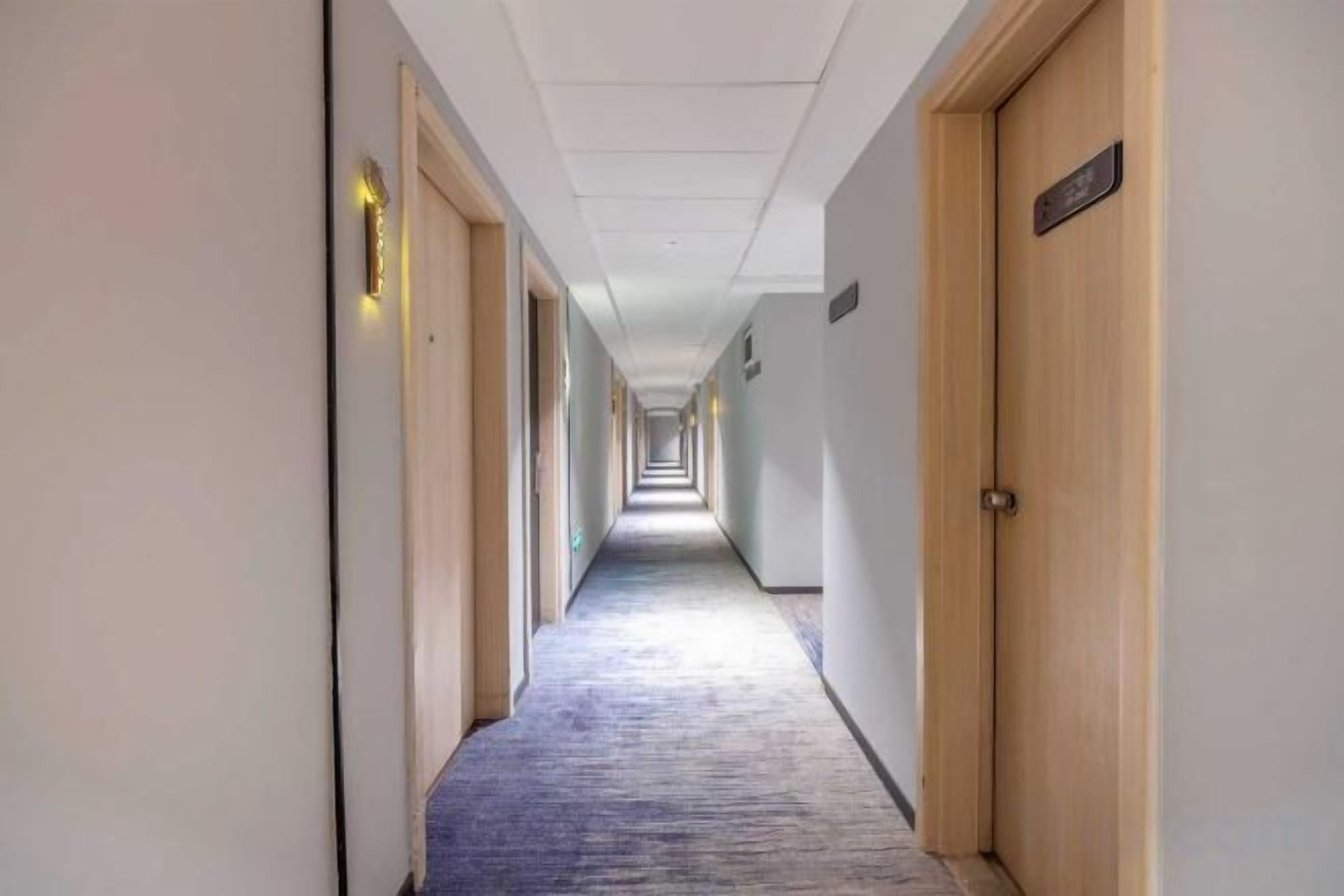 Un pasillo de hotel con puertas a ambos lados, pisos alfombrados y un techo de color claro.