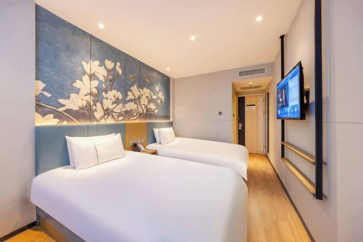A hotel room with two beds, a large wall painting, a television, and a wooden floor.