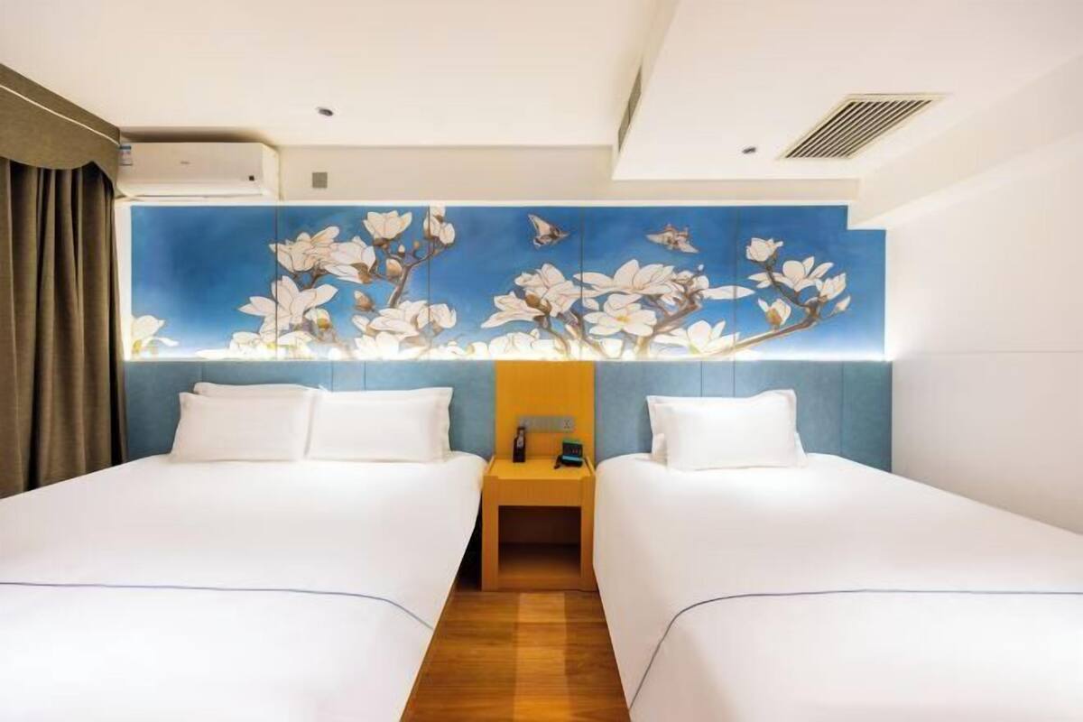 A hotel room with two beds, a nightstand, and a wall mural.