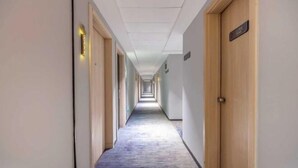 Pitkä, kapea hotellikäytävä, jonka molemmilla puolilla on puiset ovet ja jonka lattia on peitetty matolla.