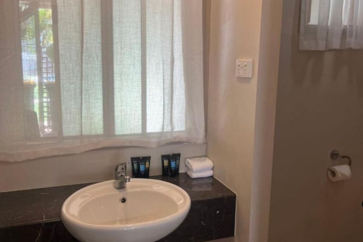 A bathroom with a white sink, a window with sheer curtains, and a towel on the counter.