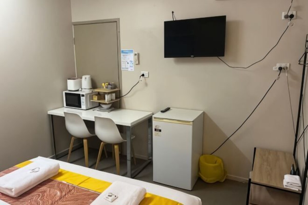 A hotel room with a bed, a desk with a microwave, a small refrigerator, a TV, and a chair.