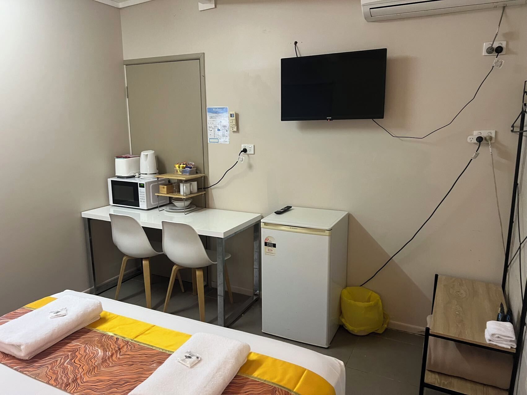 A small, compact hotel room with a bed, a desk with a microwave, a TV, and a small fridge.