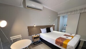 Quarto de hotel com cama, mesa de cabeceira, cadeira e ar condicionado.