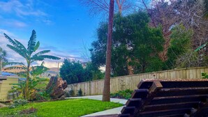 A backyard with a wooden deck, a bench, and a variety of plants and trees. - The Green Bach opposite beach- quirky and great for groups and families (Ōmāpere)