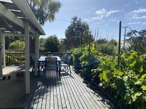 Una terraza de madera con una mesa y sillas, rodeada de exuberante follaje y un cielo despejado.
