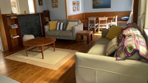 A cozy living room with a sofa, armchair, wooden coffee table, and a bookshelf. - The Green Bach opposite beach- quirky and great for groups and families (Ōmāpere)