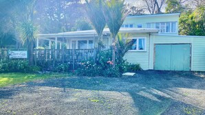 A guest house with a covered porch, a fenced garden, and a gravel driveway. - The Green Bach opposite beach- quirky and great for groups and families (Ōmāpere)