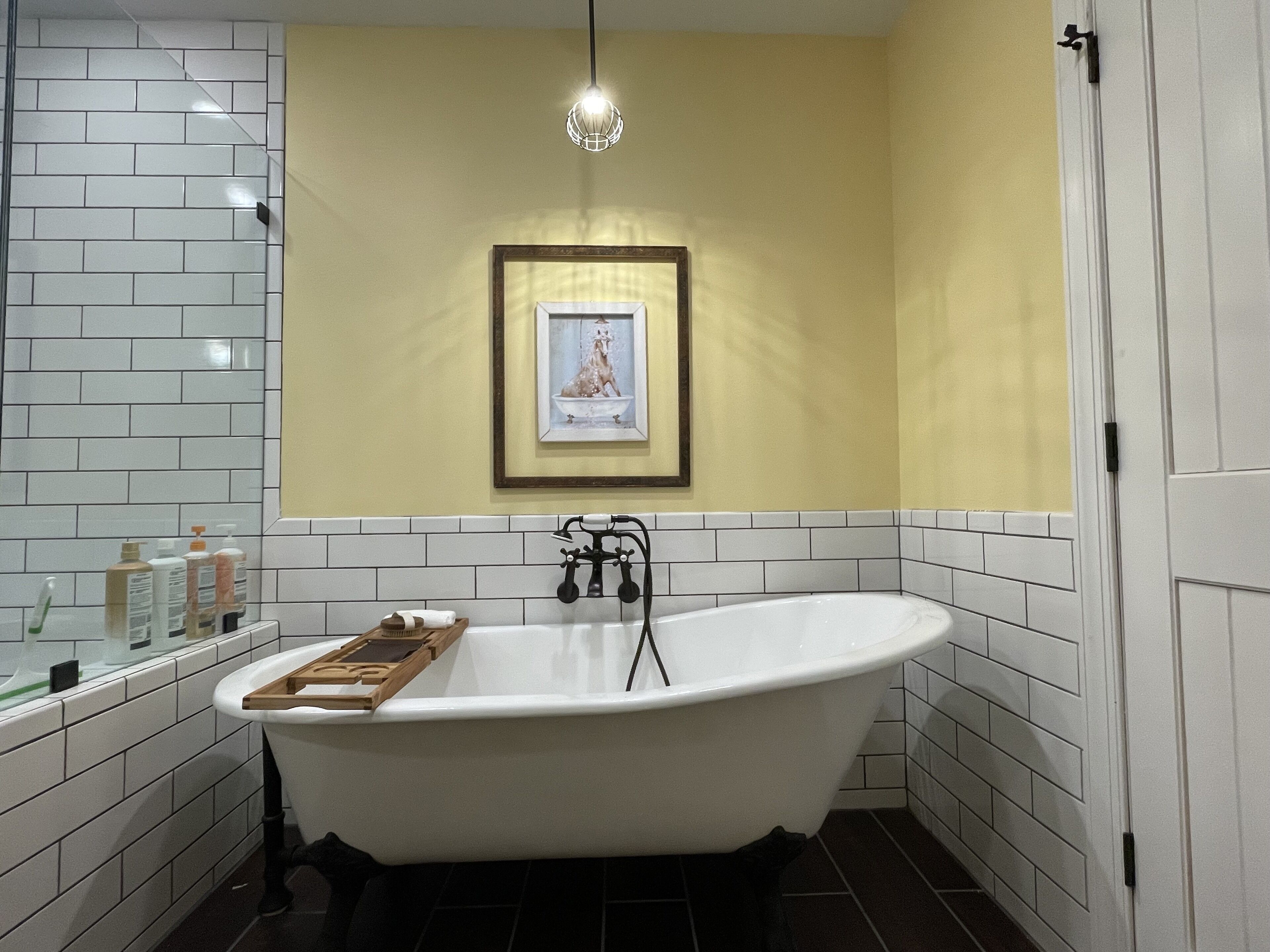 A bathroom with a freestanding bathtub, a framed picture on the wall, and toiletries on the counter.