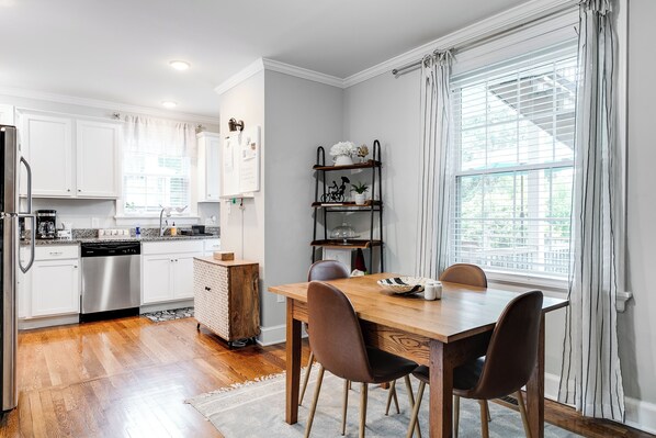 Una cocina moderna con armarios blancos, lavavajillas de acero inoxidable y una mesa de comedor de madera con sillas.