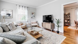 A modern living room with a sofa, coffee table, TV, and a bookshelf. - 2-bedroom villa minutes from Carytown, VCU, UofR, & Richmond Convention Center (Richmond)