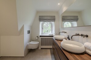 A modern bathroom with a toilet, a window, a vanity with two sinks, and a radiator.