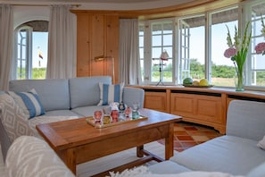 Ein gemütliches Wohnzimmer mit einer Couch, einem Holztisch und Blick ins Freie durch große Fenster.