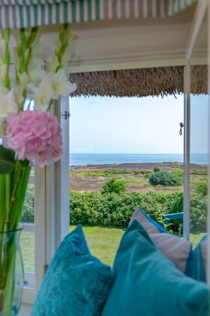 Ein Zimmer mit Meerblick, einem Strohdach und einem Fenster zum Garten.