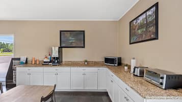 Een moderne keuken met witte kasten, granieten werkbladen, een ingebouwde magnetron, broodrooster en koffiezetapparaat. Er hangen ingelijste foto's aan de muur en staat een kleine plant op het aanrecht.