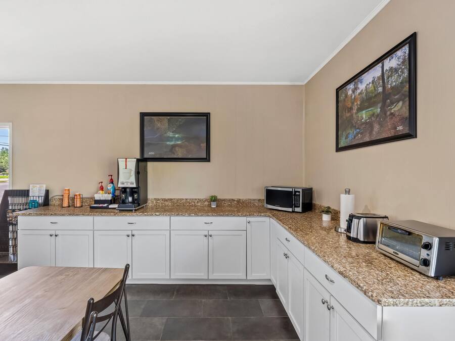 Een moderne keuken met witte kasten, granieten werkbladen, een ingebouwde magnetron, broodrooster en koffiezetapparaat. Er hangen ingelijste foto's aan de muur en staat een kleine plant op het aanrecht.