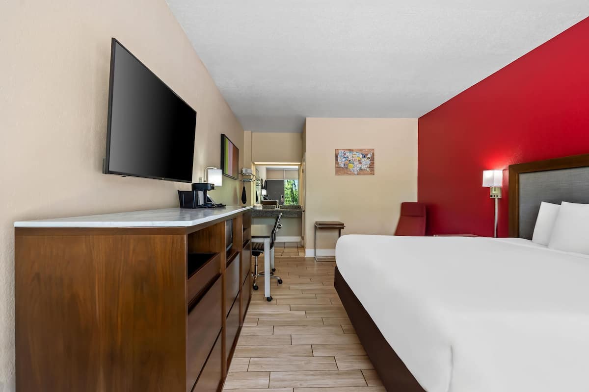 Ein Hotelzimmer mit Bett, Schreibtisch, Flachbildfernseher, Stuhl und einem kleinen Tisch.