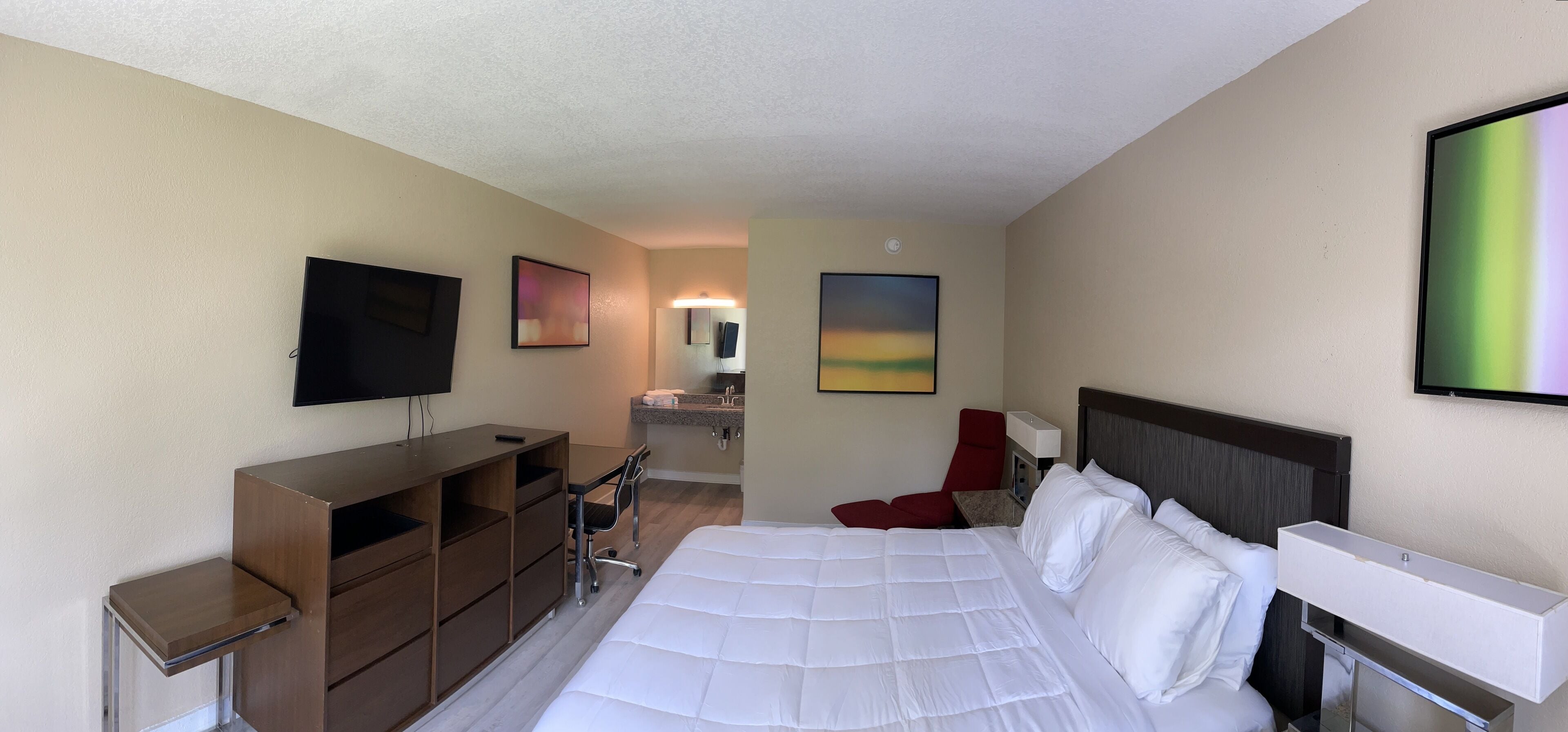 A hotel room with a bed, a desk, a chair, a TV, and artwork on the walls.
