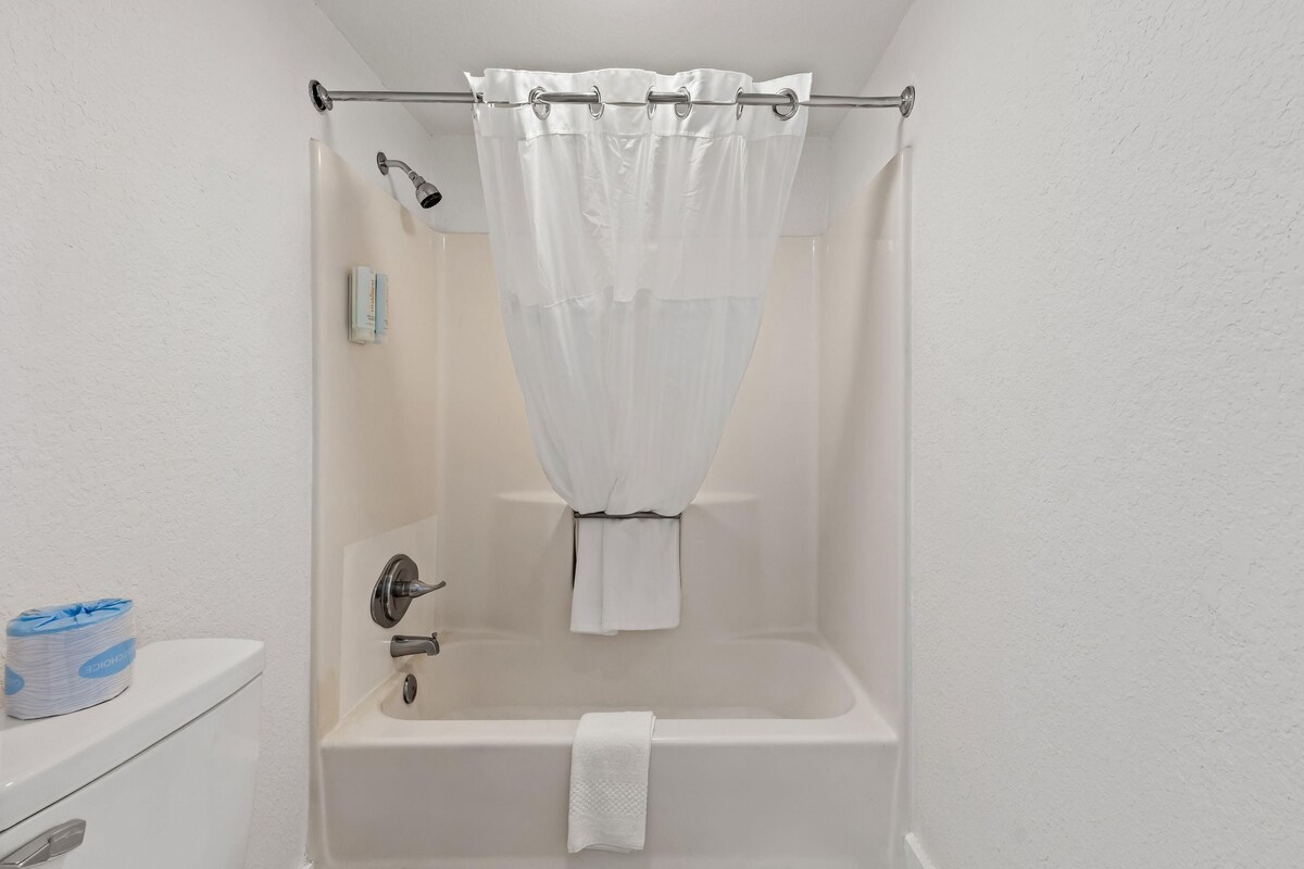 A bathroom with a bathtub, a shower curtain, a towel, and a toilet paper dispenser.