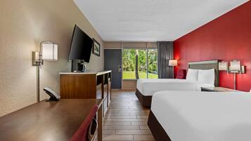 Une chambre d’hôtel avec deux lits, un bureau, une télévision et une fenêtre donnant sur un espace verdoyant.