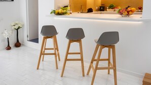 Een moderne keuken met een wit aanrecht, drie grijze barkrukken en een fruitschaal.