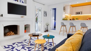 Een moderne woonkamer met een open haard, een aan de muur bevestigde televisie en een keuken met barstoelen.