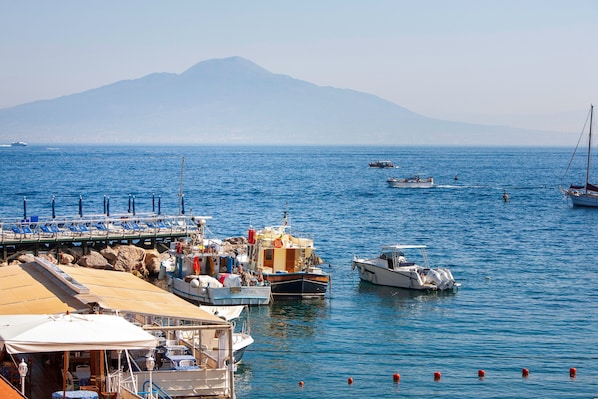 A marina with boats docked, a pier with chairs, and a mountain in the background.