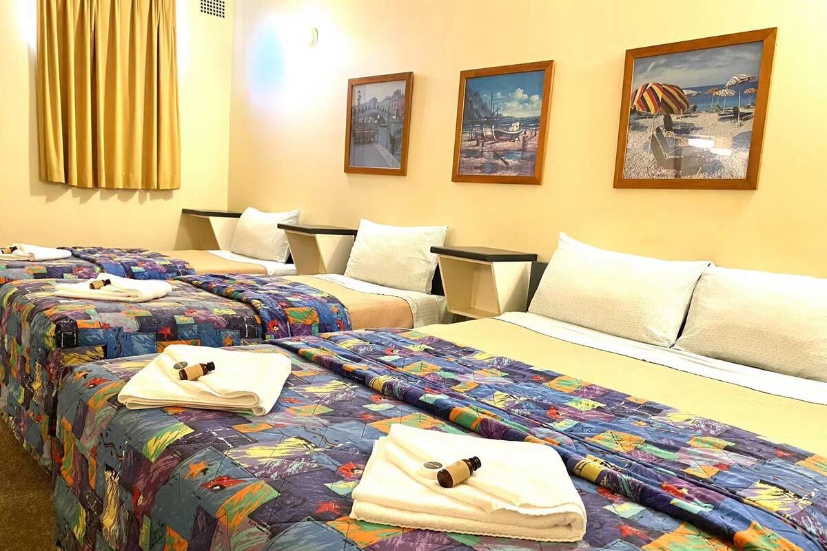 Ein Hotelzimmer mit zwei Betten, jedes mit farbenfrohen Bettdecken und Handtüchern. An der Wand hängen drei gerahmte Bilder.