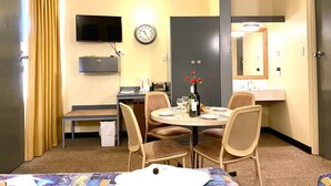 Une chambre d’hôtel équipée d’une table à manger, de chaises, d’un téléviseur, d’une horloge, d’un miroir et d’un mini-bar.