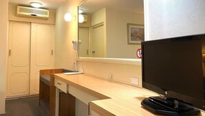 Une chambre d’hôtel avec un bureau en bois, un grand miroir, un téléviseur à écran plat et un sèche-cheveux fixé au mur.