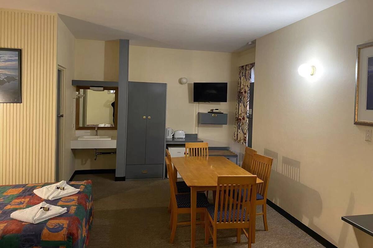 Ein Hotelzimmer mit Bett, einem Holztisch mit Stühlen, einem Fernseher, einem Schreibtisch mit Computer und einem Kleiderschrank.