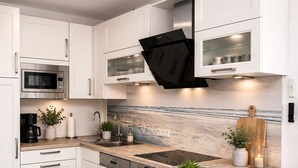 Una cocina moderna con armarios blancos, una isla central con taburetes y un horno empotrado, además de un salpicadero con una escena de playa.